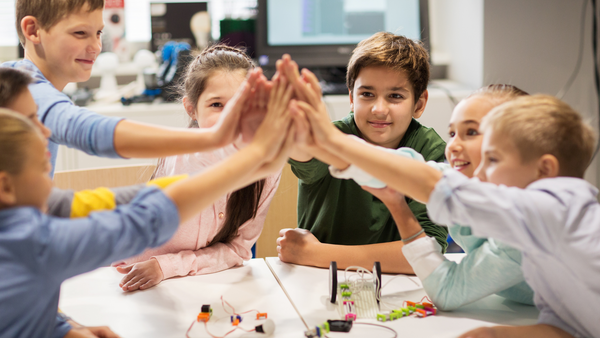 A group of young students high-five each other at a working table in their classroom while the build with littleBits.