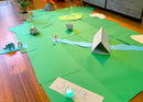 Mini golf course made out of construction paper and household items in a living room.