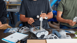A student works on a RVR+ robot with a wind sensor on top.