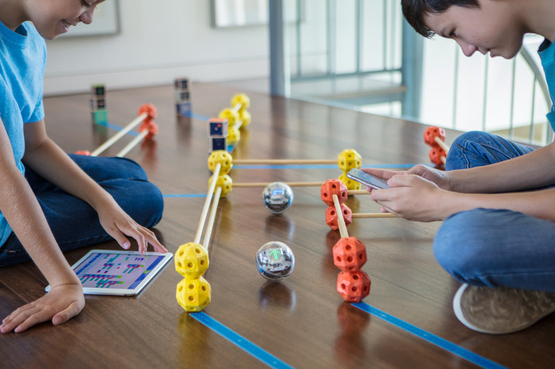 Two boys program their Sphero BOLT robots through a maze build out of a toy construction set at home.