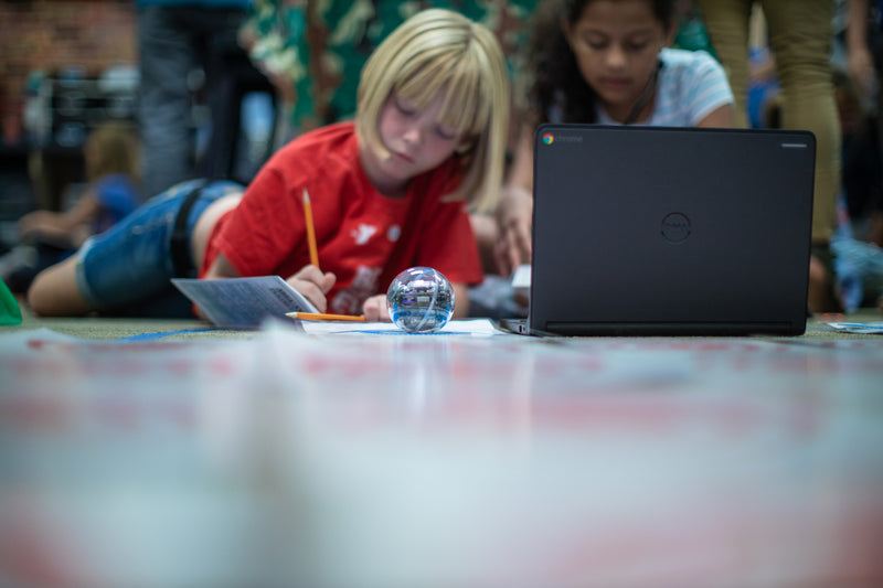 Two young girl students work together on a project using a laptop and Sphero BOLT.