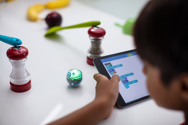 Young boy coding Sphero Mini on his tablet through salt and pepper grinder.