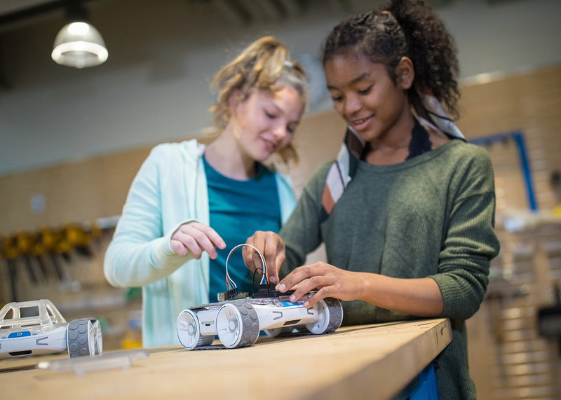 Two teenage girls work together in a makerspace to build an invention on top of their Sphero RVR.