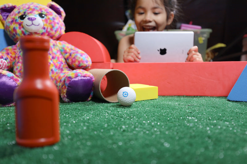 A young girl codes her Sphero Mini Golf ball with a tablet.