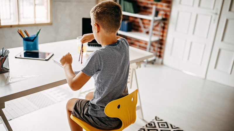 A boy sits at his desk at home and works independently on an assignment.