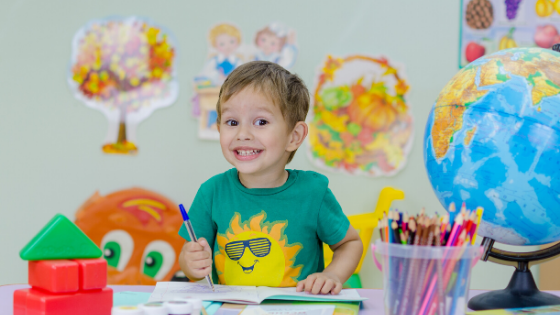 Child smiling at camera sitting at arts and crafts table. 