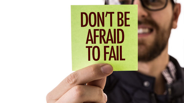 A man holds a small sign that reads "Don't be afraid to fail."