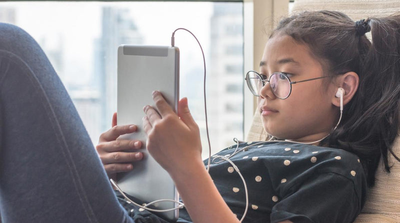 Young girl sits in chair while looking at a tablet.