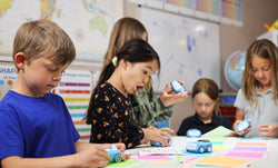 A group of young students work together to program Sphero indi with color tiles in a classroom.