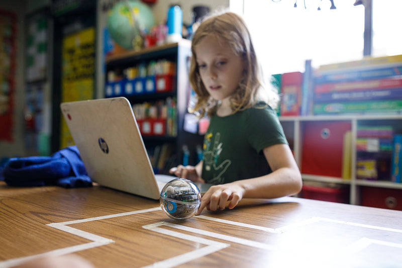 A girl programs her Sphero BOLT with a laptop by herself.