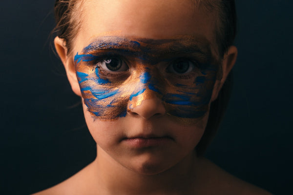 Child with paint on face looking straight at camera.