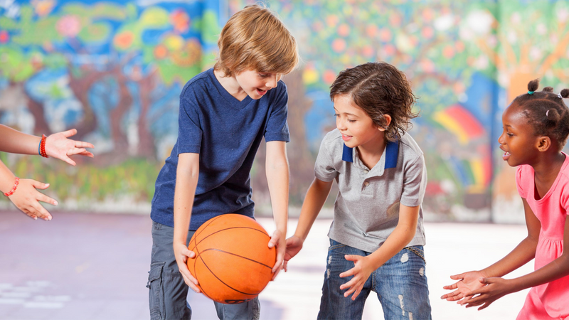 Two boys and a girl pass a basketball to each other in gym class.
