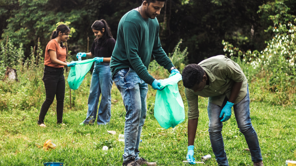Four people pick up trash in a field to create a cleaner environment around them.