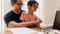 Young boy and father sit at desk while learning off a laptop together. 