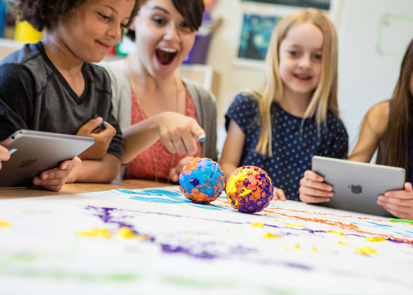 An excited teacher and students pointing to a robot ball covered in paint. 