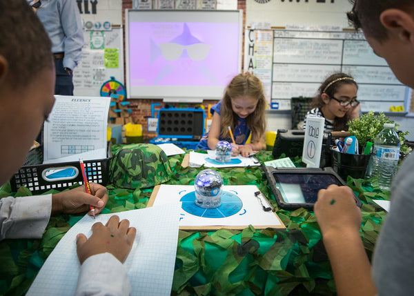 Students sitting around a table working on a science project using a toy robot ball. 