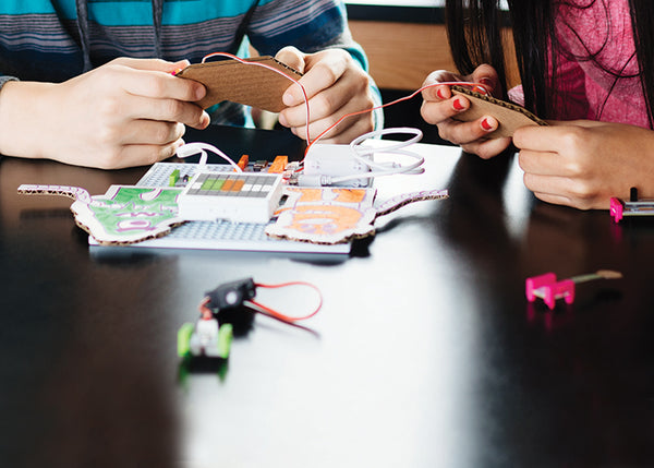 A girl and boy inventing with electronic snap-together building blocks. 