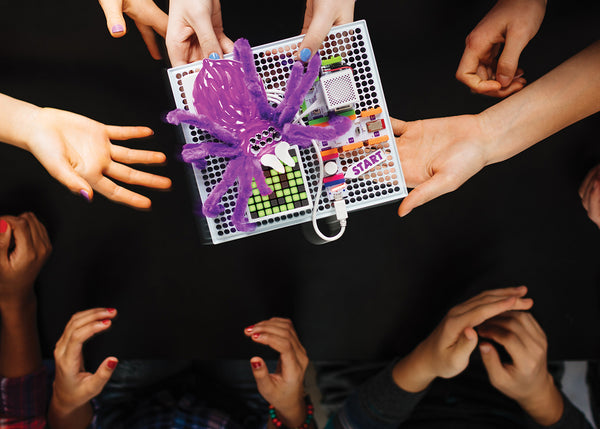 A group of hands holding a completed littleBit's spider invention. 