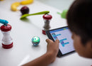 Kid programming robotic ball through salt and pepper shakers on a table.