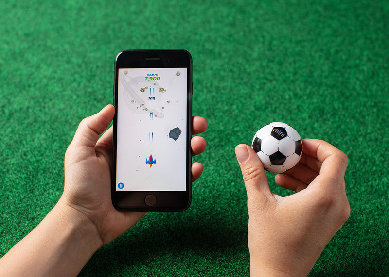 Mini Soccer being used as a game controller next to a smartphone with a space game on the screen.