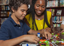 Teacher and student putting together littleBits near a bookshelf.
