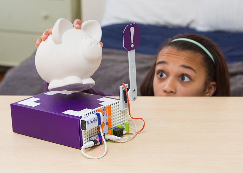 Girl having fun playing with piggy bank and littleBits invention.